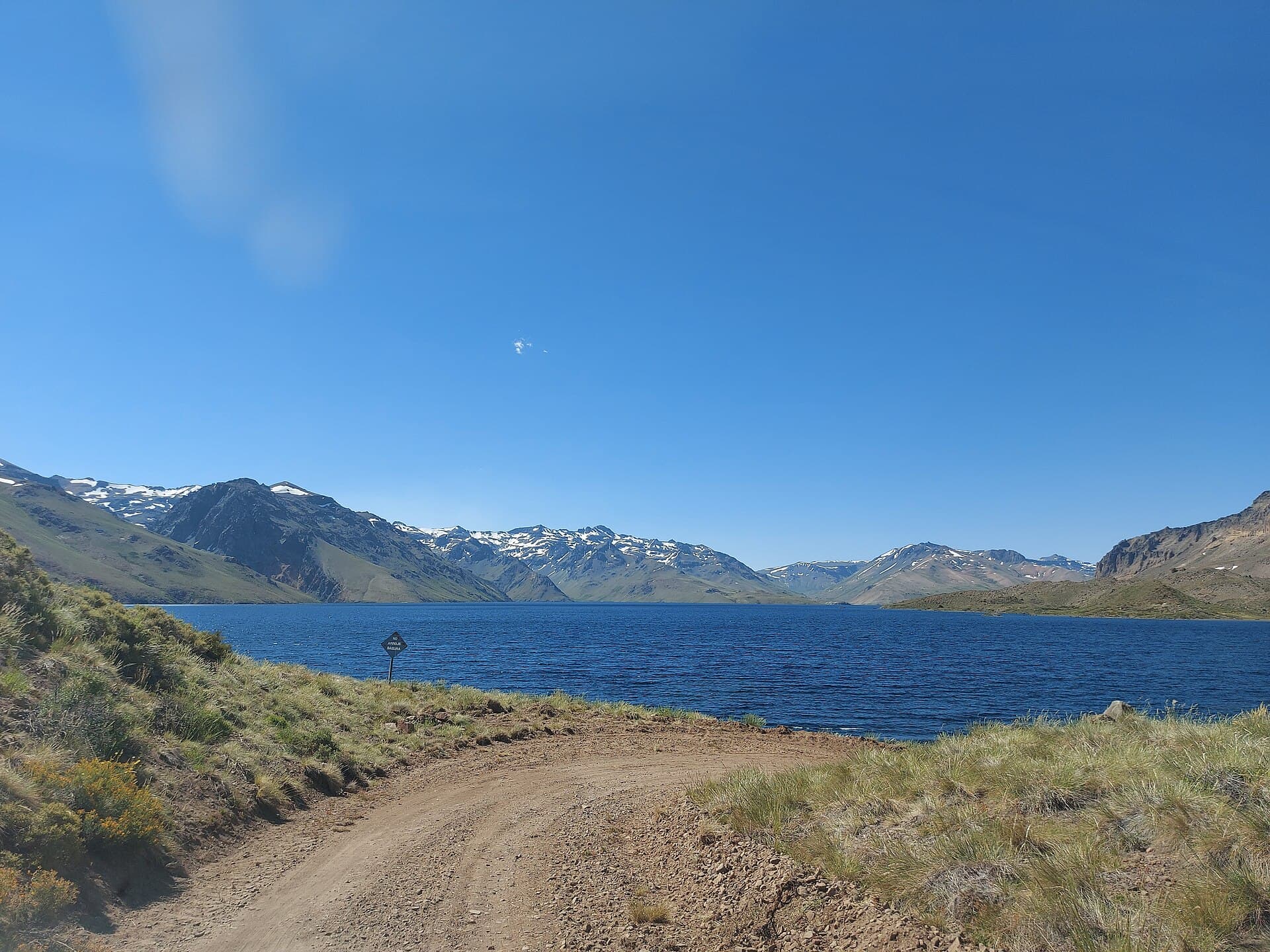 La laguna Varvarco Campos, el camino de ripio y los cordones nevados al fondo